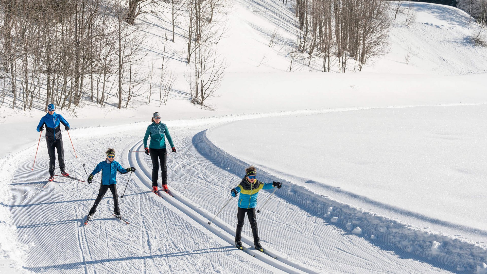 Familie beim Langlauf auf verschneiter Loipe im sonnigen Winterwald