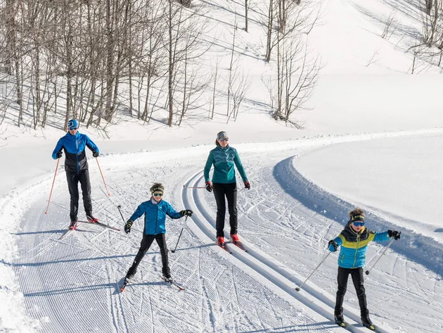 Familie beim Langlauf auf verschneiter Loipe im sonnigen Winterwald