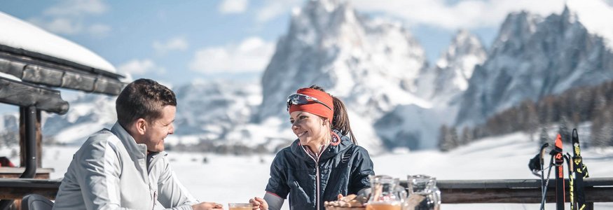 Best of Dolomitenregion Seiser Alm © Dolomiti Nordic Ski - Manuel Kottersteger Paar beim Frühstück im Freien mit Schneelandschaft und Bergen im Hintergrund