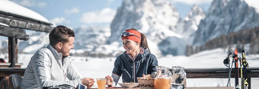 Paar beim Frühstück im Freien mit Schneelandschaft und Bergen im Hintergrund