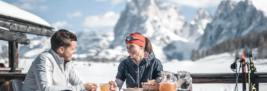 Paar beim Frühstück im Freien mit Schneelandschaft und Bergen im Hintergrund