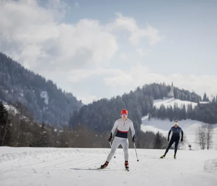 Ratschings © Ratschings Tourismus - Manuel Kottersteger Zwei Langläufer auf verschneiter Loipe vor bewaldeten Bergen