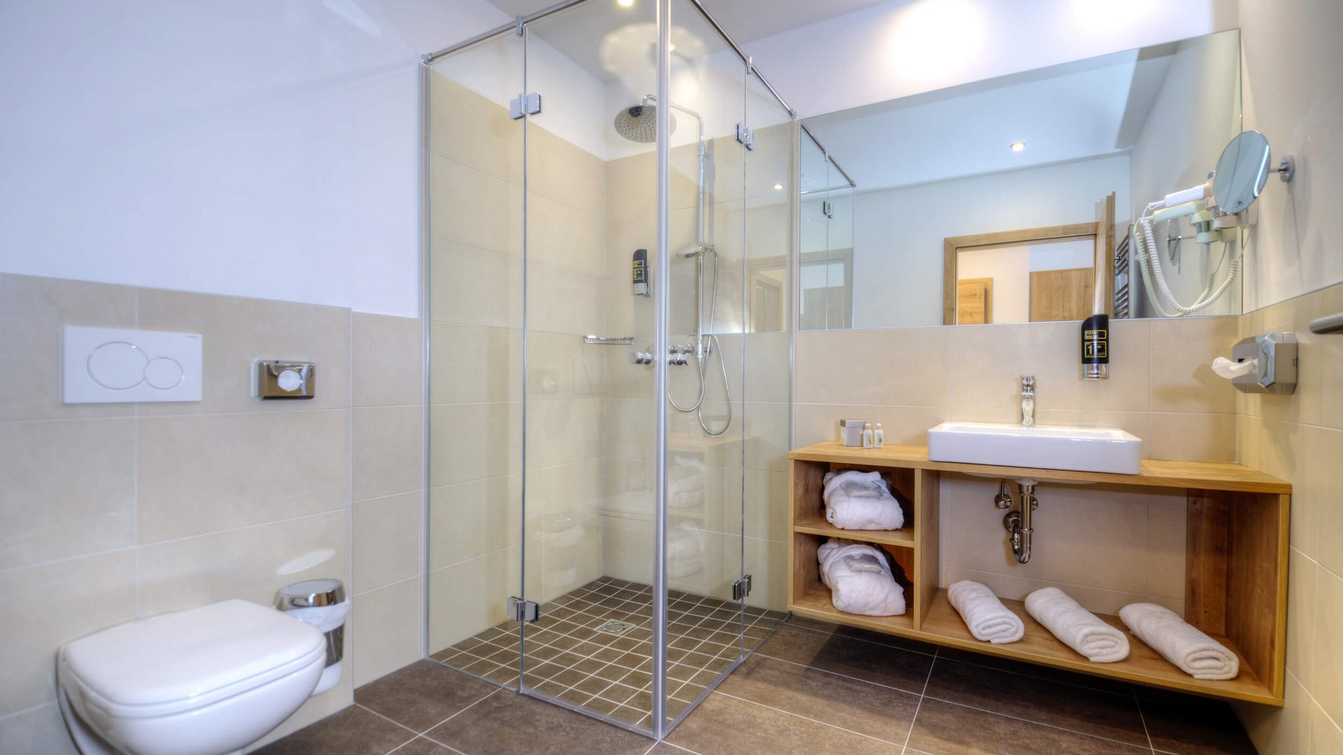 Modern bathroom with glass shower, toilet, sink, and towels on wooden shelves