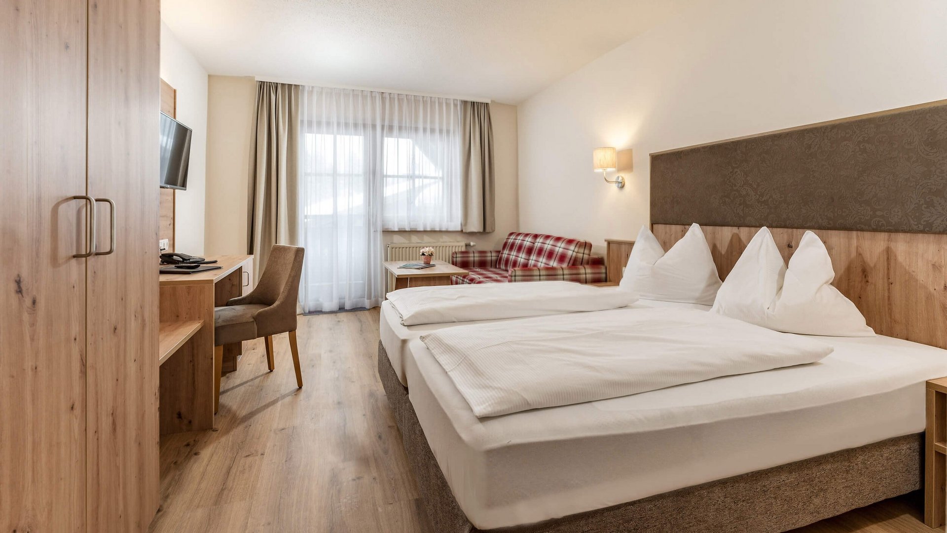 Cozy hotel room with double bed, desk, and sofa near window with curtains