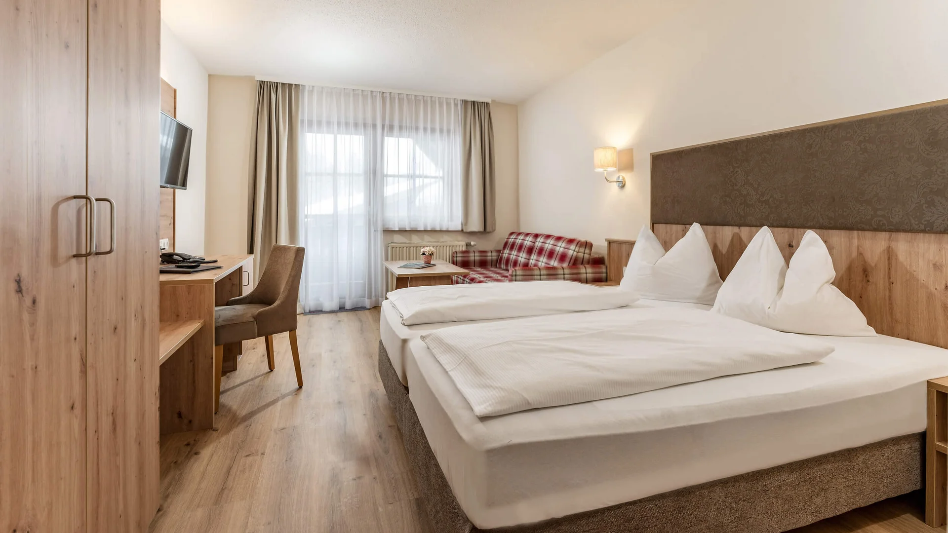 Hotel Sonnenhügel **** © Hotel Hanneshof GmbH Cozy hotel room with double bed, desk, and sofa near window with curtains
