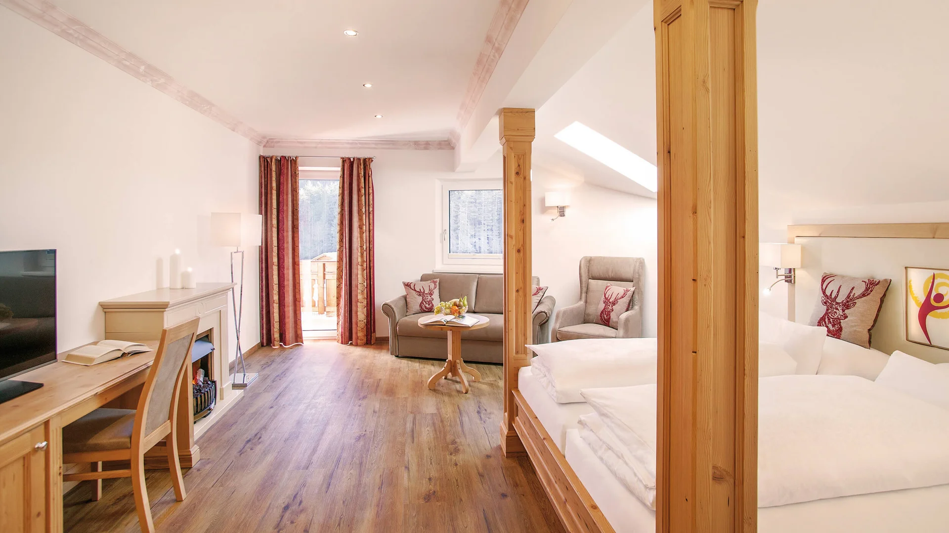 Alpenhotel Karwendel **** © Hotel Karwendel Bernhard Rödlach BetriebsGmbH Helles Wohnzimmer mit Holzmöbeln und roten Vorhängen