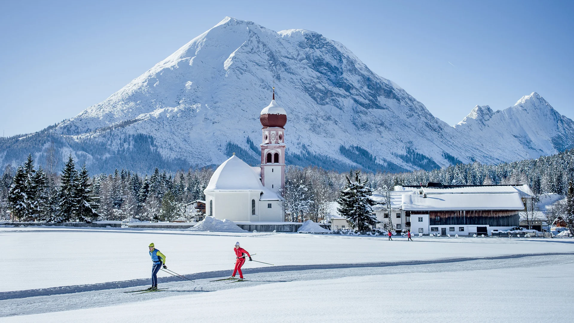 Langlaufopening in Leutasch © Region Seefeld - Hannes Dabernig Langläufer vor einer Kirche und einem verschneiten Bergpanorama