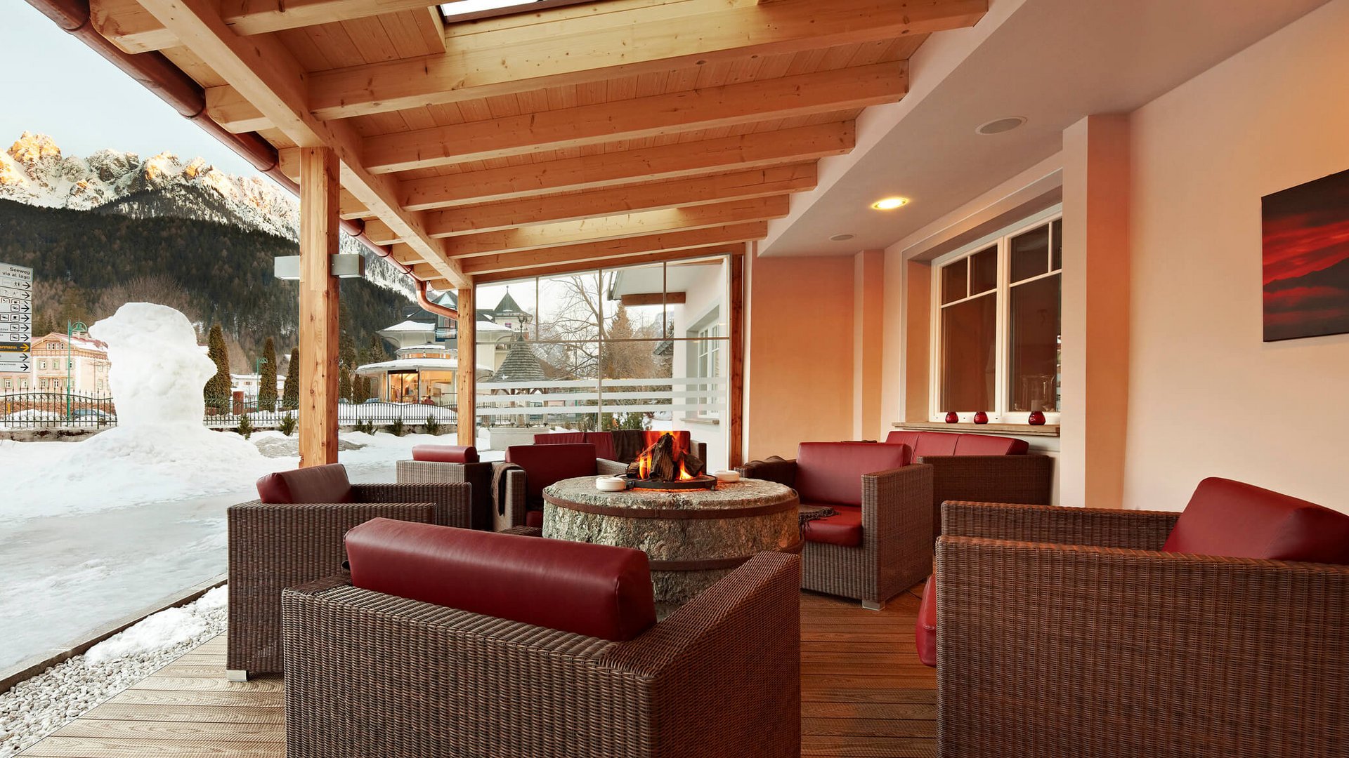 Überdachte Sitzgruppe mit Kamin vor schneebedeckten Bergen und Schneedekoration
