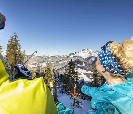 Zwei Wanderer blicken auf schneebedeckte Berge und Heißluftballons im Himmel