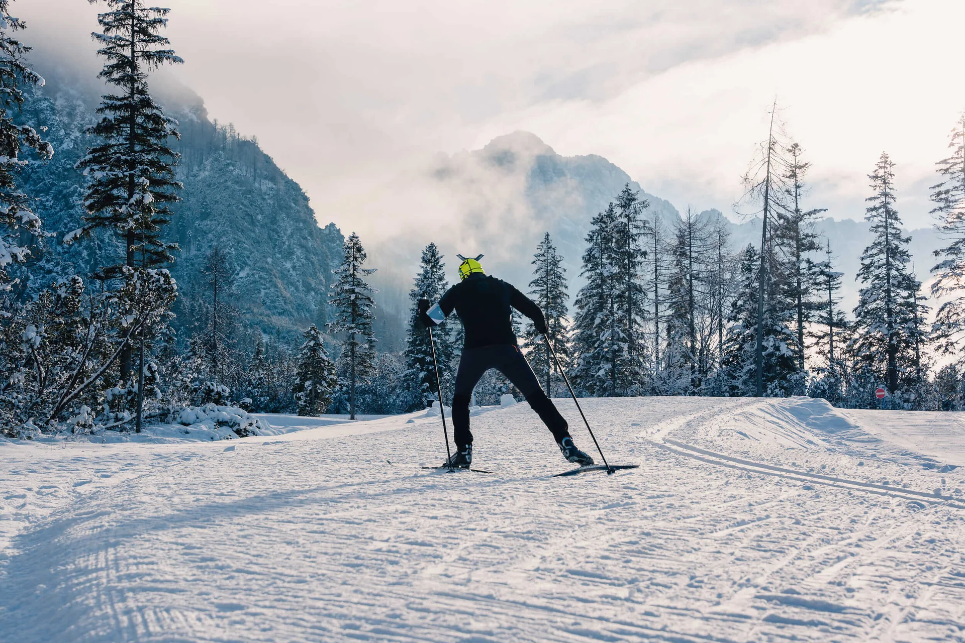 Langläufer unterwegs im Schnee vor bewaldeten Bergen bei Dämmerung