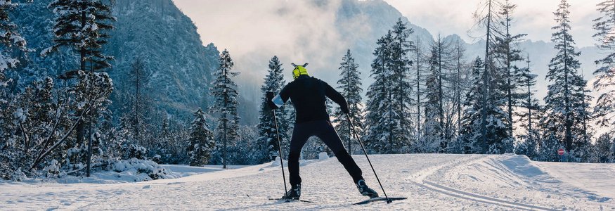 Langläufer unterwegs im Schnee vor bewaldeten Bergen bei Dämmerung