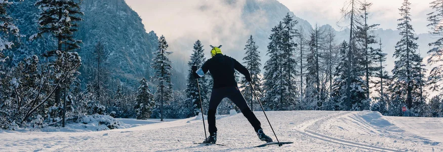 Langläufer unterwegs im Schnee vor bewaldeten Bergen bei Dämmerung