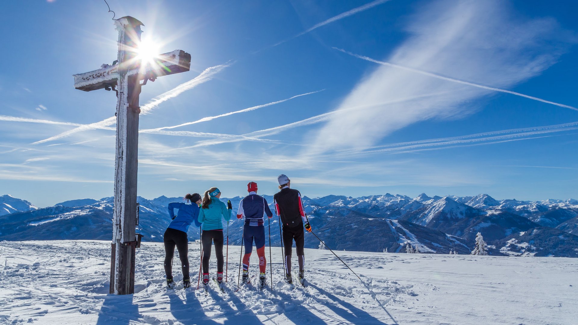 Four cross-country skiers by a summit cross on a sunny winter day in the mountains