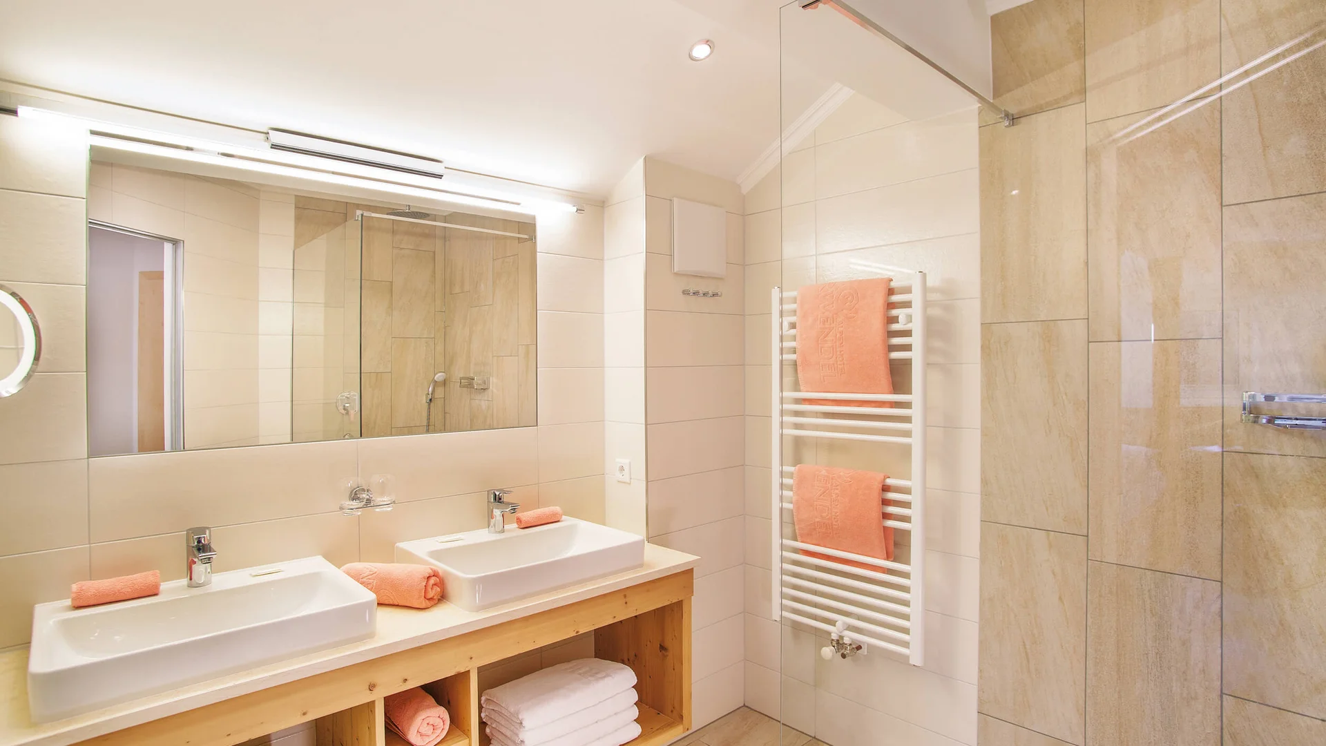 Alpenhotel Karwendel **** © Hotel Karwendel Bernhard Rödlach BetriebsGmbH Modernes Badezimmer mit Doppelwaschbecken und orangefarbenen Handtüchern