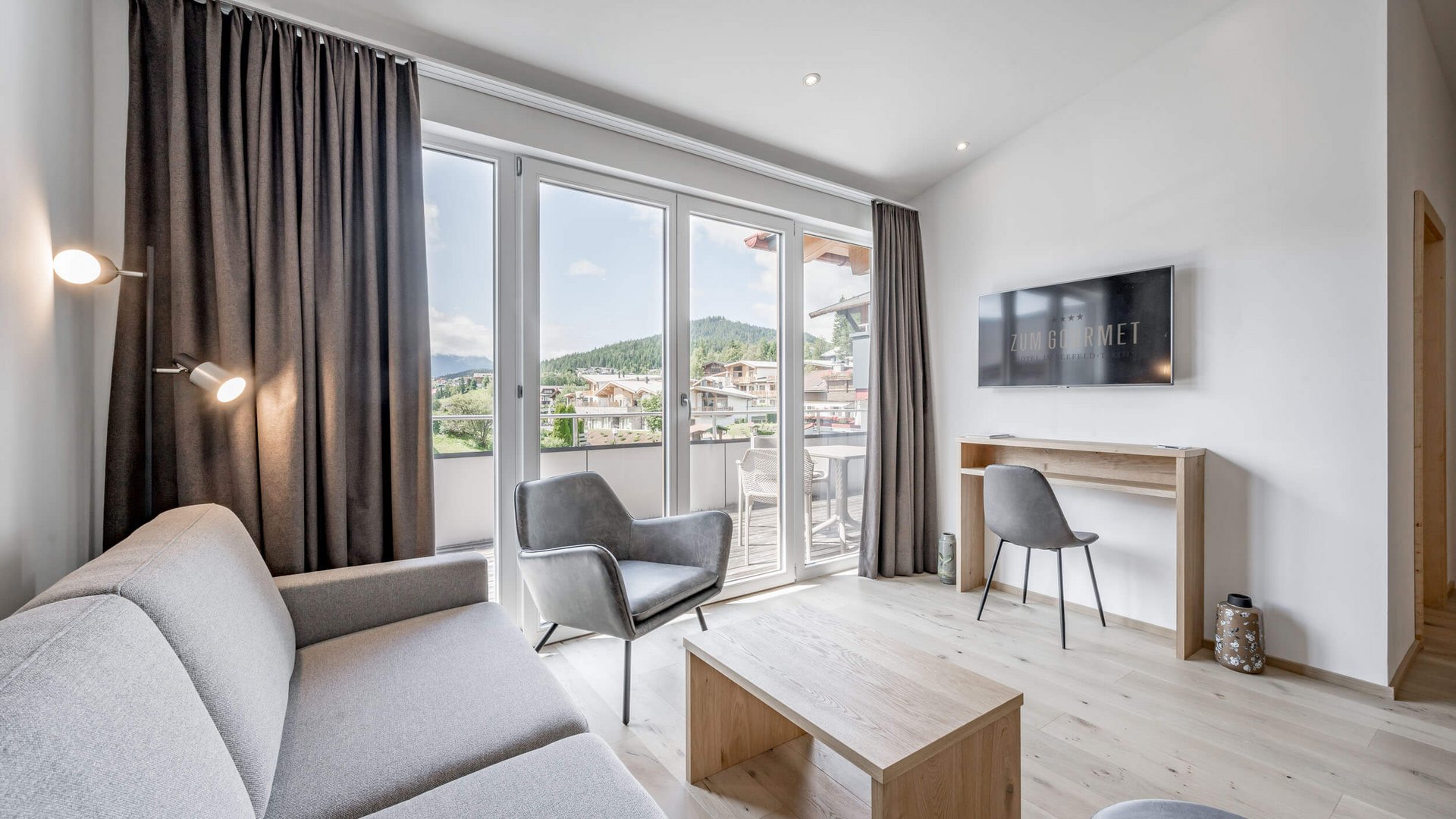 Modern living room with gray sofa, armchair, TV, and balcony with mountain view