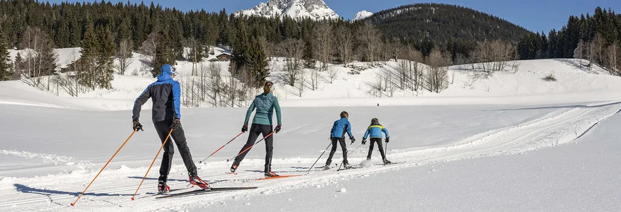 Hotel Sonnenhügel **** © Lorenz Masser - Filzmoos Tourismus Four people cross-country skiing in snowy mountain landscape on clear day