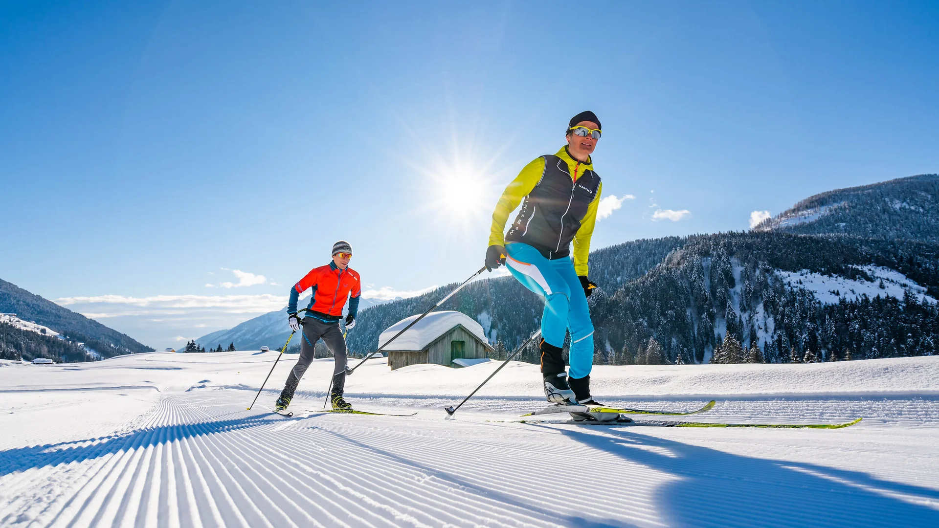 Zwei Langläufer auf sonniger, frisch präparierter Skipiste in den Bergen