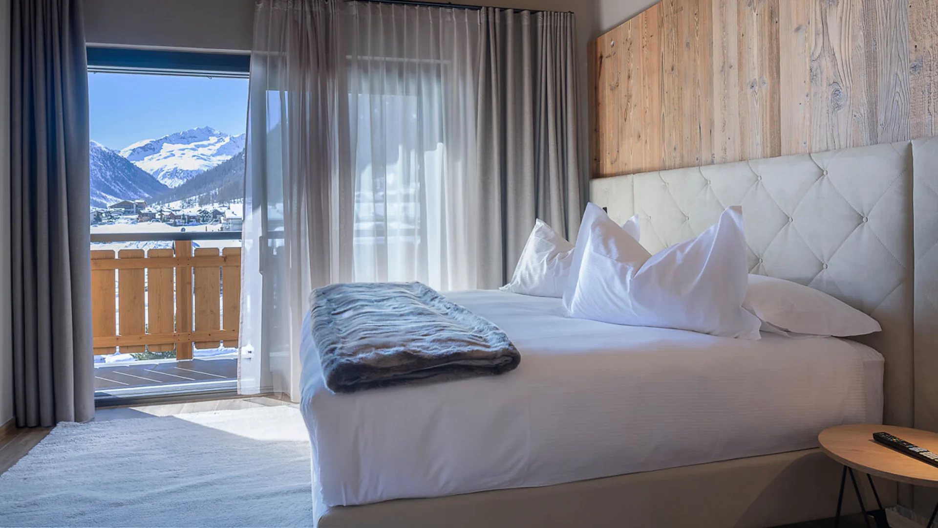Modern hotel room with bed and mountain view through glass sliding door