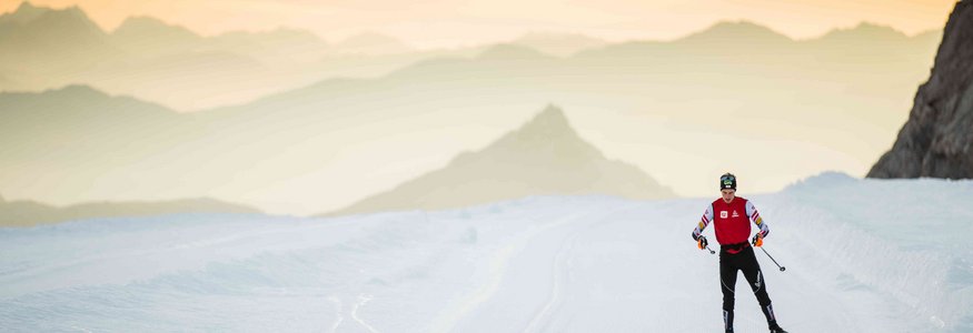 Langläufer auf schneebedeckter Strecke mit Bergen im Sonnenuntergang