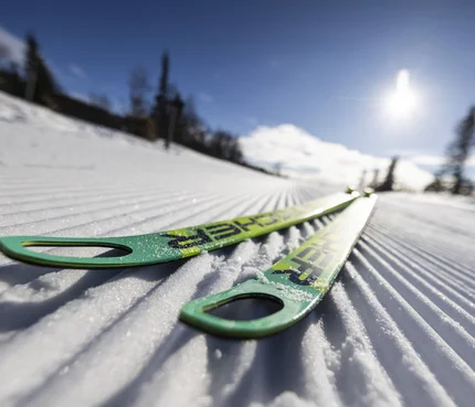 Grüne Skier liegen auf frisch präparierter Loipe im Sonnenschein