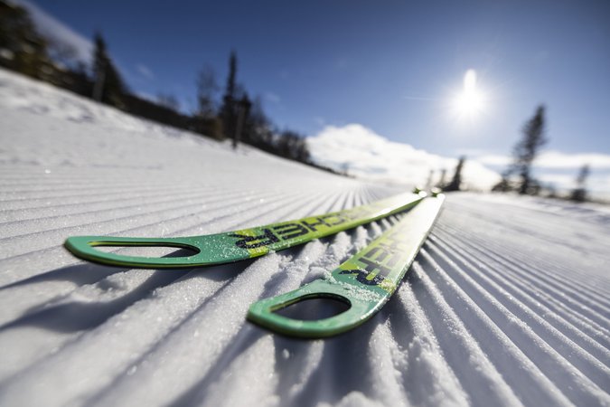 Grüne Skier liegen auf frisch präparierter Loipe im Sonnenschein