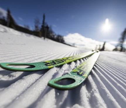 Grüne Skier liegen auf frisch präparierter Loipe im Sonnenschein