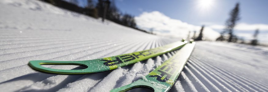 Grüne Skier liegen auf frisch präparierter Loipe im Sonnenschein