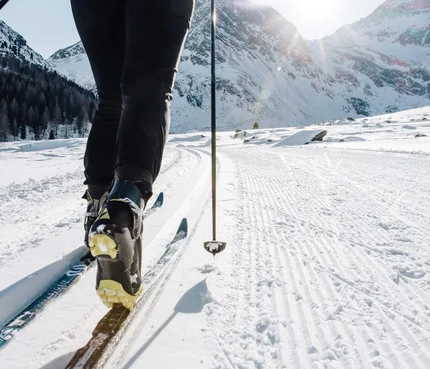 Person beim Langlaufen auf verschneiter Strecke mit Berglandschaft im Hintergrund
