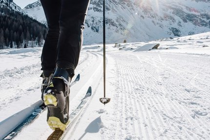 Person beim Langlaufen auf verschneiter Strecke mit Berglandschaft im Hintergrund
