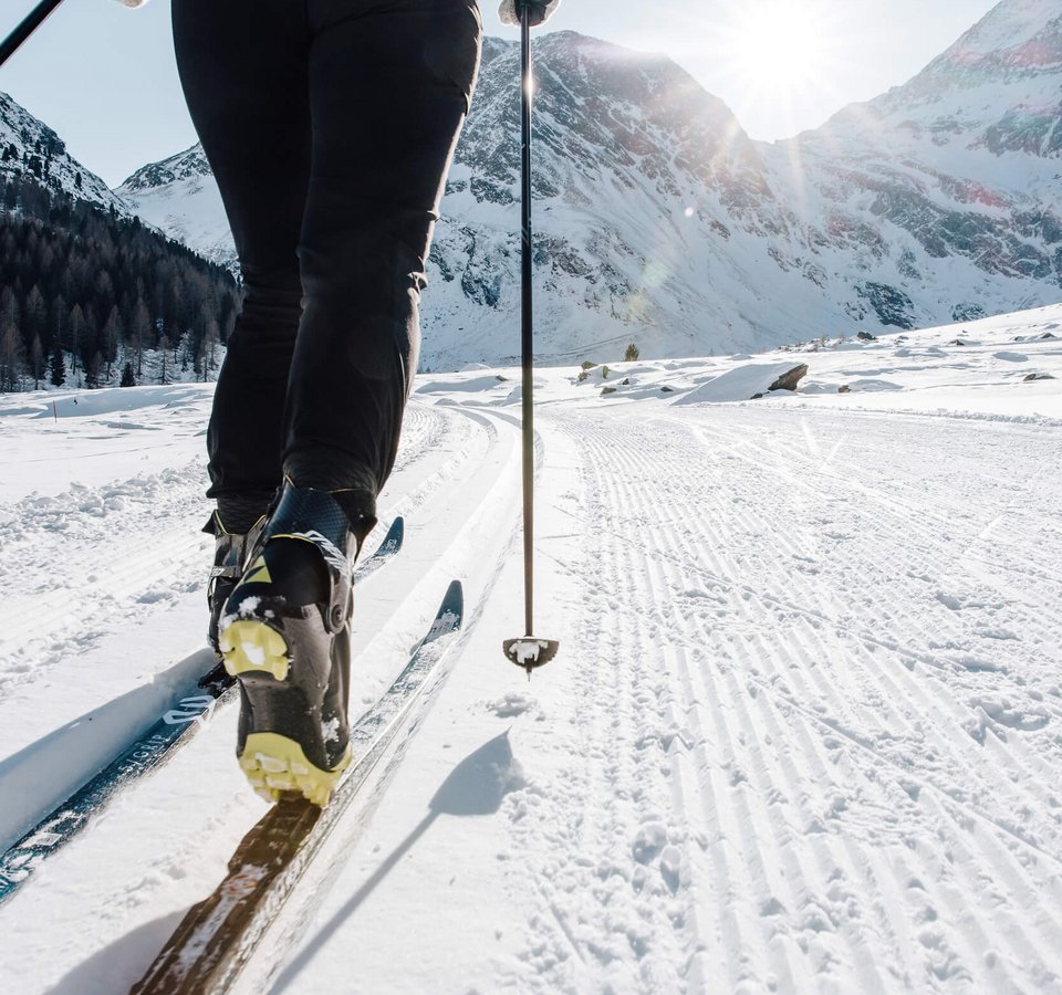 Person beim Langlaufen auf verschneiter Strecke mit Berglandschaft im Hintergrund
