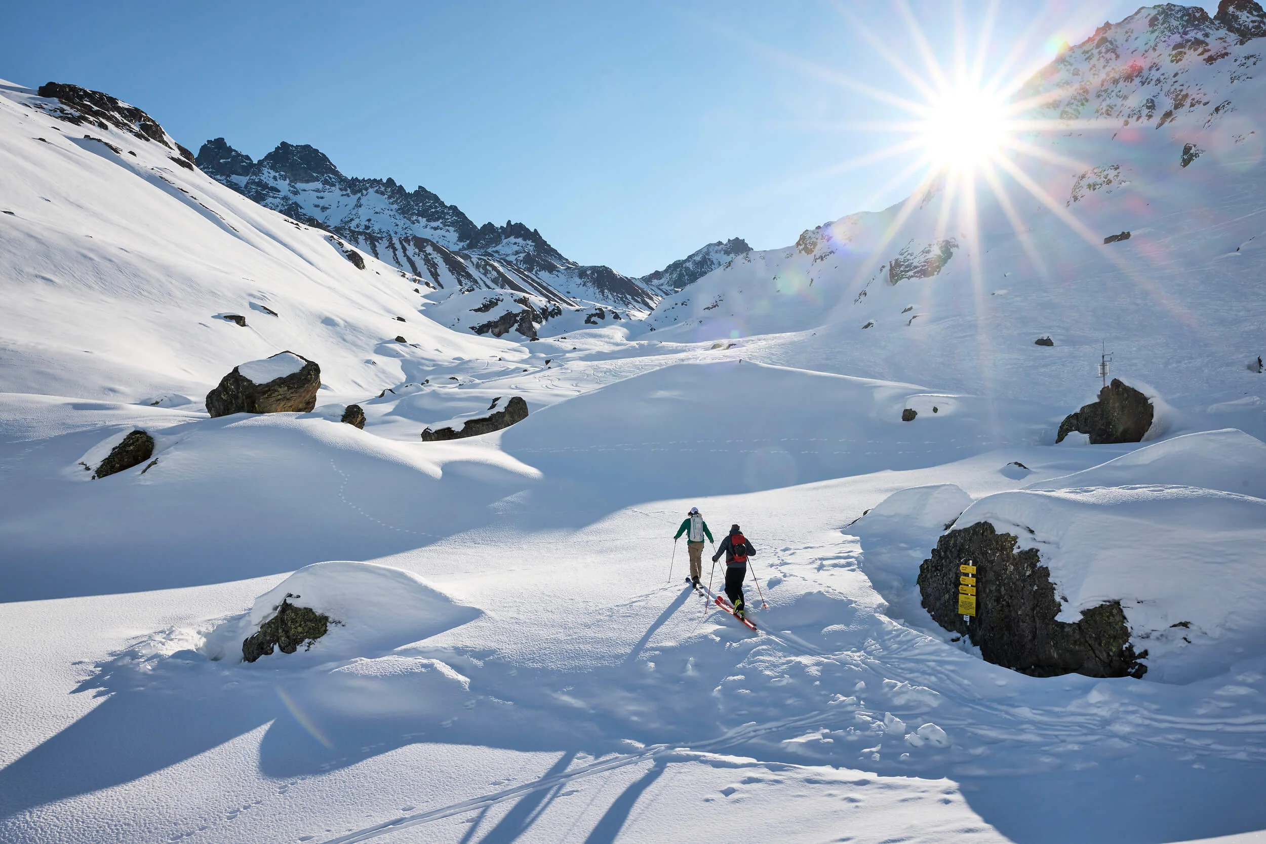 Zwei Skifahrer wandern bei Sonnenschein durch verschneite Berglandschaft