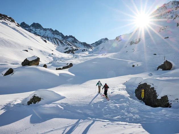 Two skiers hiking in sunny snowy mountain landscape