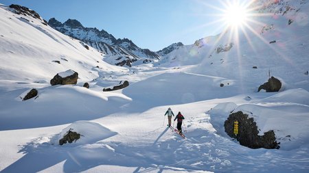 Zwei Skifahrer wandern bei Sonnenschein durch verschneite Berglandschaft