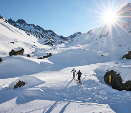 Zwei Skifahrer wandern bei Sonnenschein durch verschneite Berglandschaft