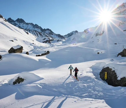 Zwei Skifahrer wandern bei Sonnenschein durch verschneite Berglandschaft