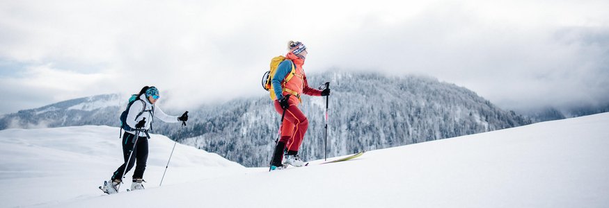 Two skiers hiking in snow with mountain background