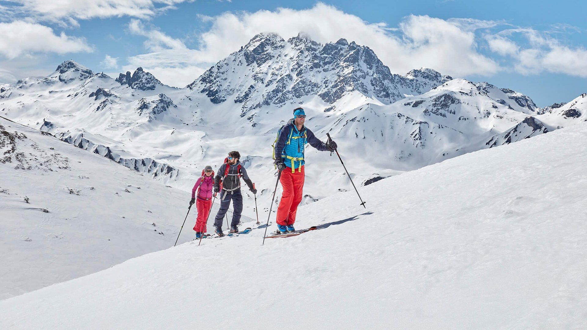 Drei Skifahrer beim Aufstieg in verschneiter Berglandschaft mit klarem Himmel