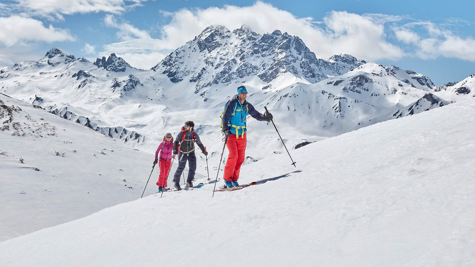 Drei Skifahrer beim Aufstieg in verschneiter Berglandschaft mit klarem Himmel
