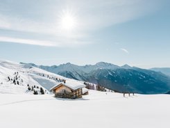Verschneites Berghaus mit Skiwanderern und sonnigem Himmel