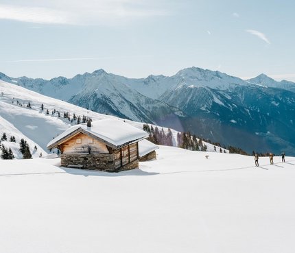 Verschneites Berghaus mit Skiwanderern und sonnigem Himmel