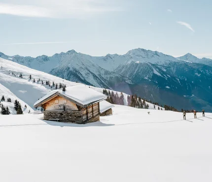 Verschneites Berghaus mit Skiwanderern und sonnigem Himmel