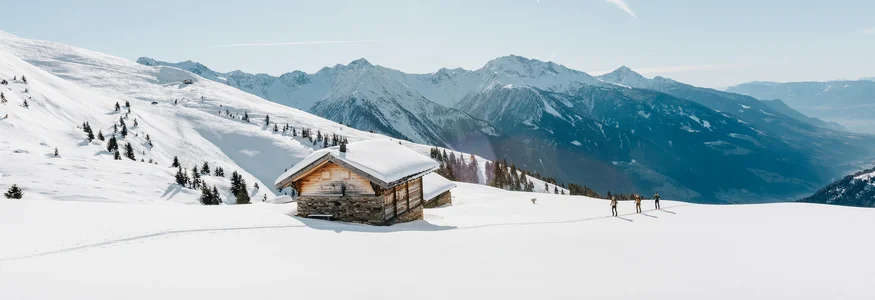 Verschneites Berghaus mit Skiwanderern und sonnigem Himmel