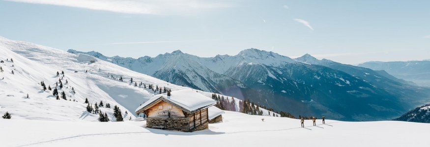 Verschneites Berghaus mit Skiwanderern und sonnigem Himmel