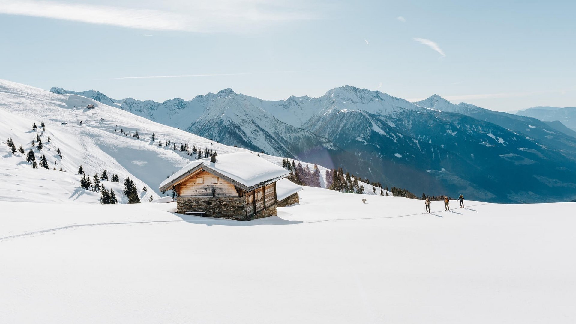 Verschneites Berghaus mit Skiwanderern und sonnigem Himmel