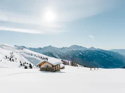 Verschneites Berghaus mit Skiwanderern und sonnigem Himmel