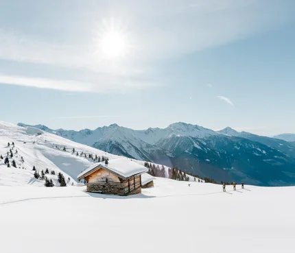 Verschneites Berghaus mit Skiwanderern und sonnigem Himmel