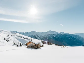 Snow-covered mountain cabin with skiers and bright sunny sky