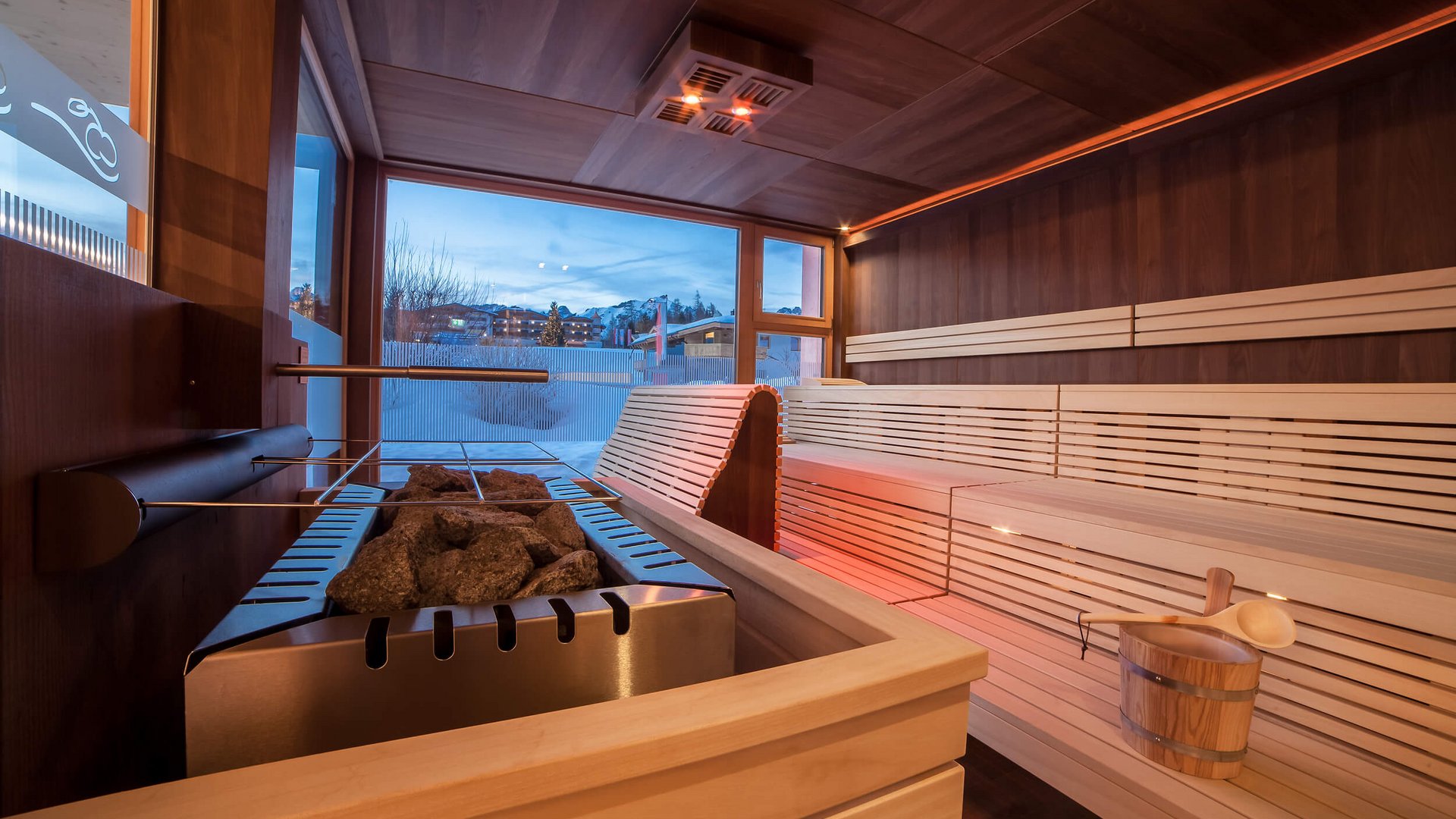 Modern sauna room with wood stove and large window showing mountain view