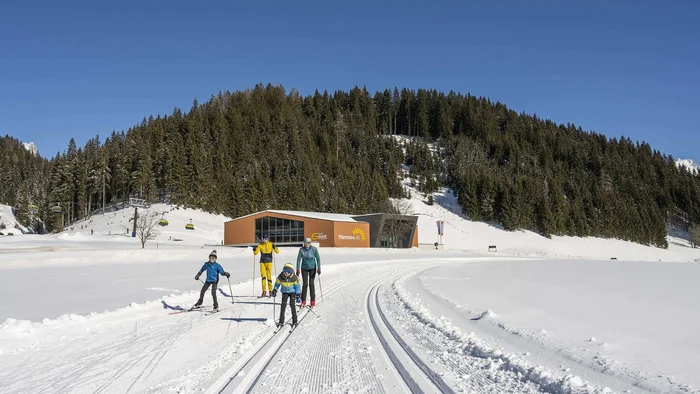 Familie beim Skilanglauf auf präparierter Loipe vor Wald und Bergstation