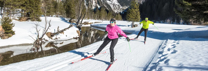Zwei Langläufer beim Ski fahren im verschneiten Gebirgstal bei Sonnenschein
